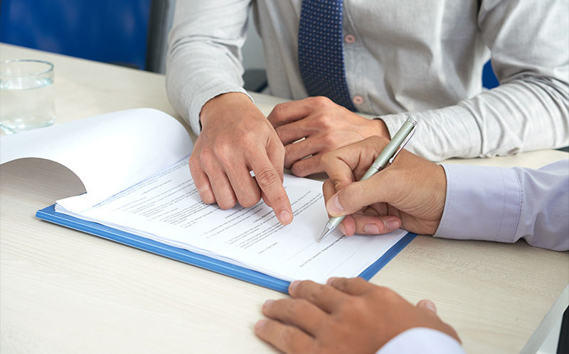 Two professionals signing a business contract on a desk.