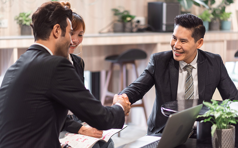 Business executive shaking hands with clients at meeting table