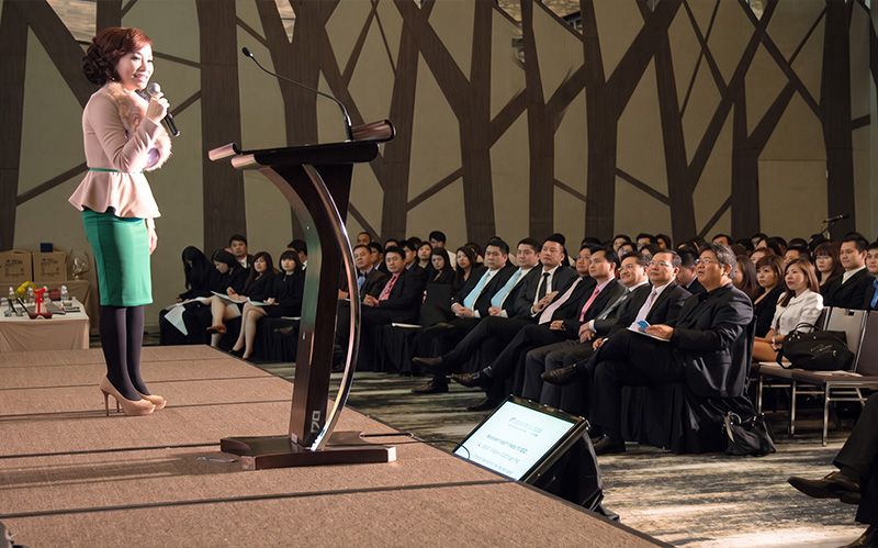 female-speaker-addressing-corporate-audience-from-stage-podium
