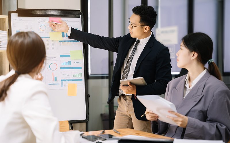 Businessman presenting data charts on a whiteboard during a team strategy meeting